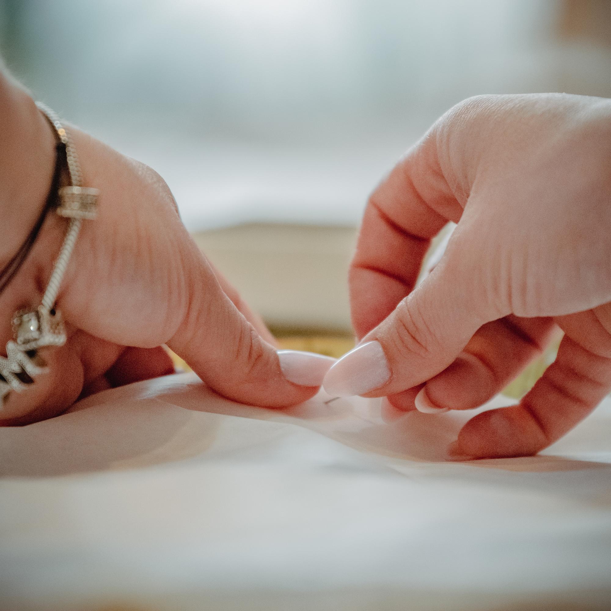 Zbliżenie ręki haftującej jedwabną nitką na naturalnej tkaninie